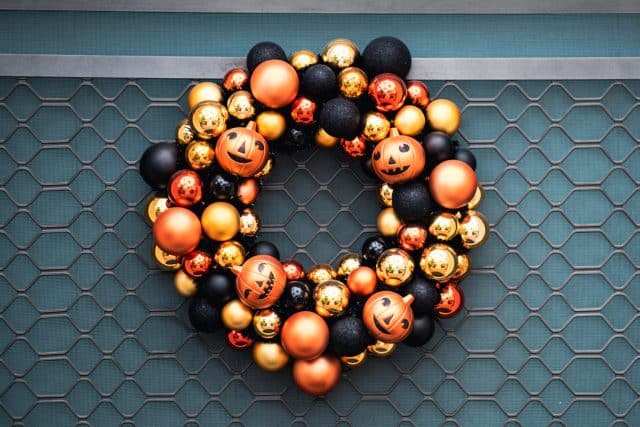 Autumn wreath on the front door with orange and black pumpkins. Scenery for Halloween in October. Decoration in the yard.