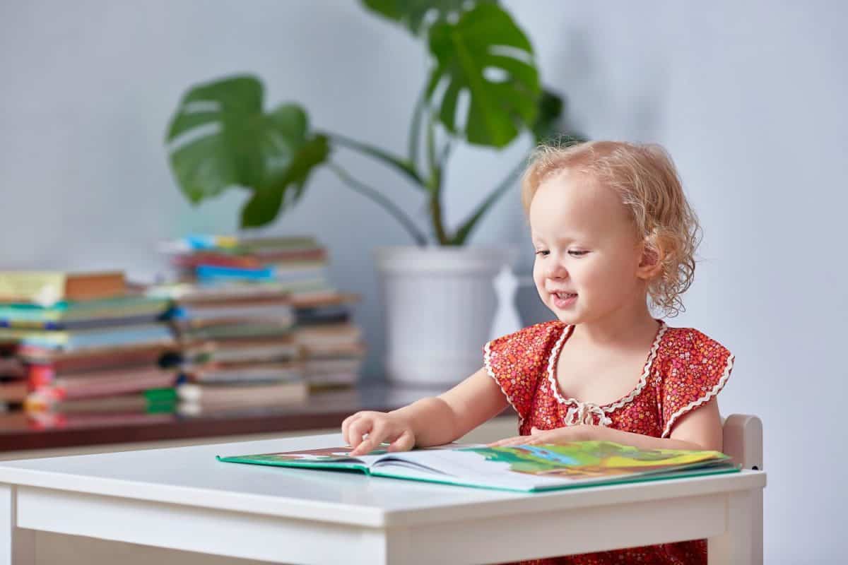 A cute girl is reading a children's book and holding a finger.