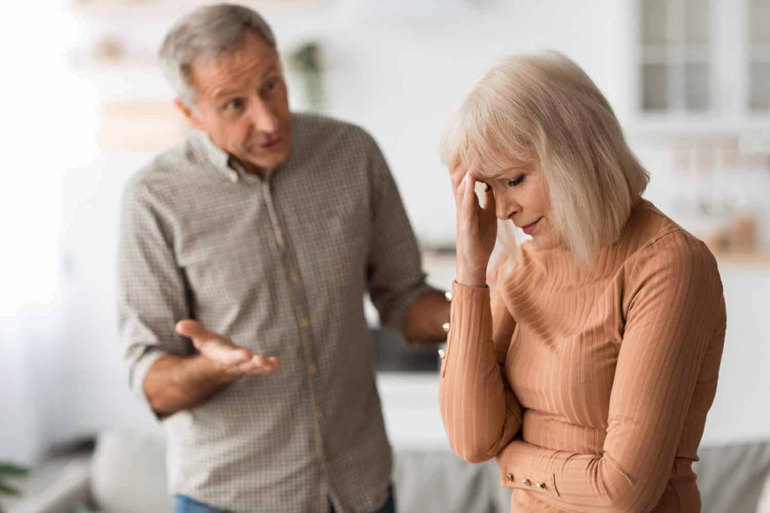 Domestic Abuse. Aggressive Senior Husband Shouting At Wife Having Quarrel Standing In Kitchen At Home. Selective Focus On Unhappy Woman. Marital Crisis And Relationship Problems Concept