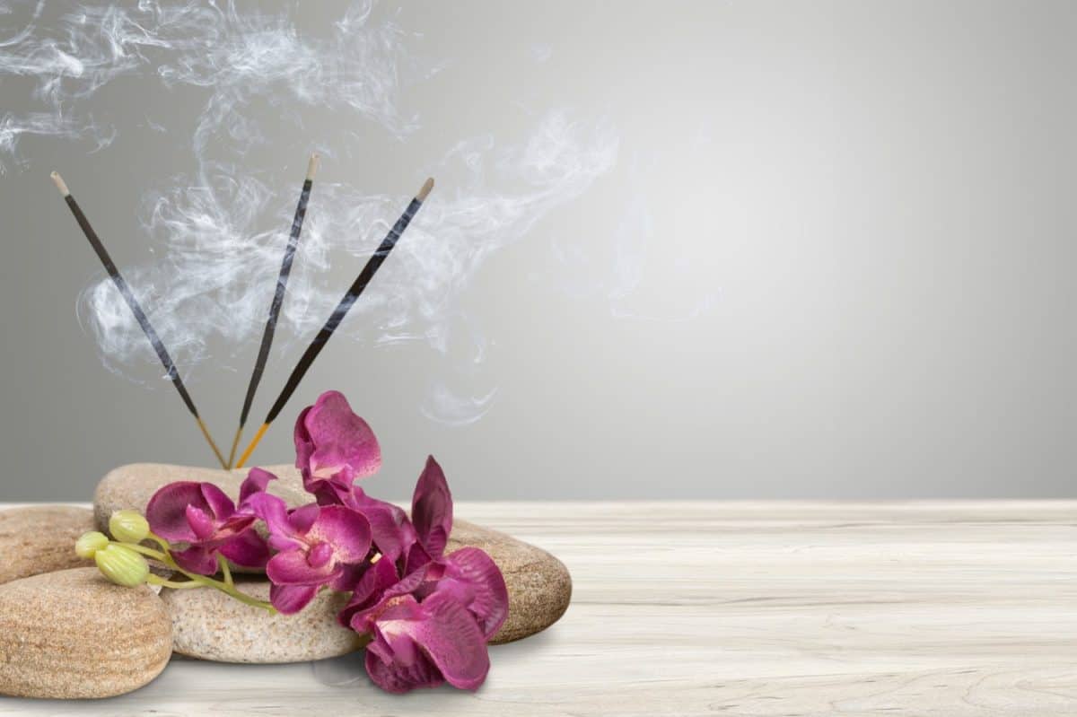 Smoke from burning incense sticks standing on holder with flowers