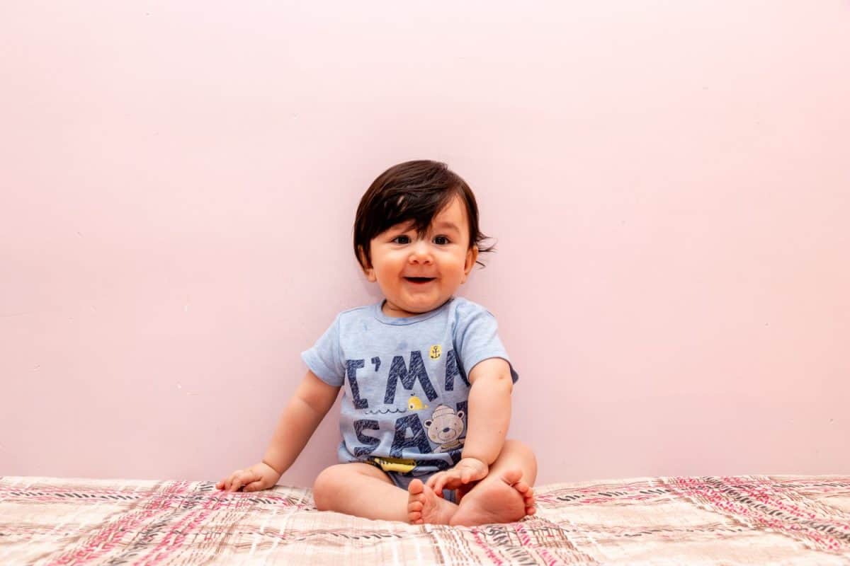 Smiling baby is sitting on the bed.Baby portrait with plain background. Cute toddler is looking lovely.