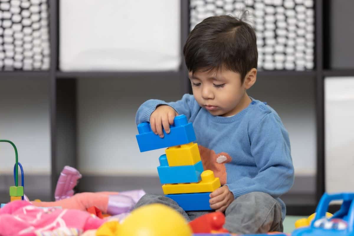 two years old mexican baby boy playing with didactic toy on messy living room