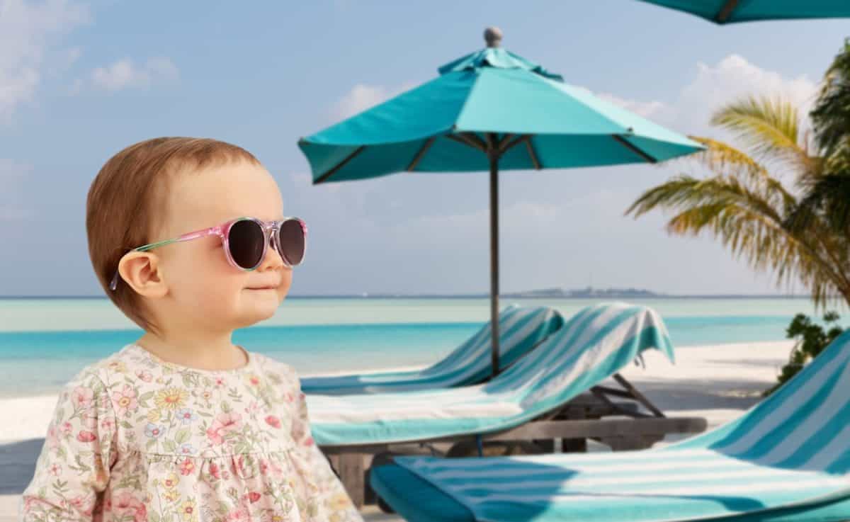 childhood, summer and people concept - happy little baby girl in sunglasses over tropical beach background in french polynesia