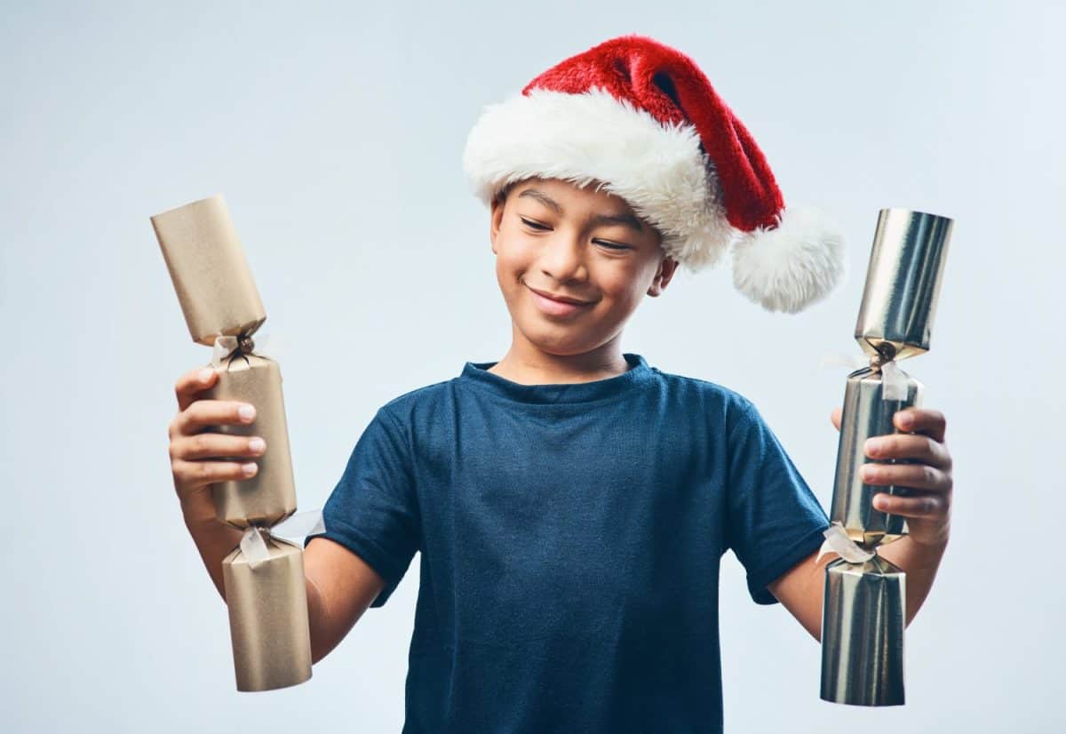 Christmas cracker explosion pending.... Studio shot of a cute little boy wearing a Santa hat and holding two Christmas crackers against a grey background.