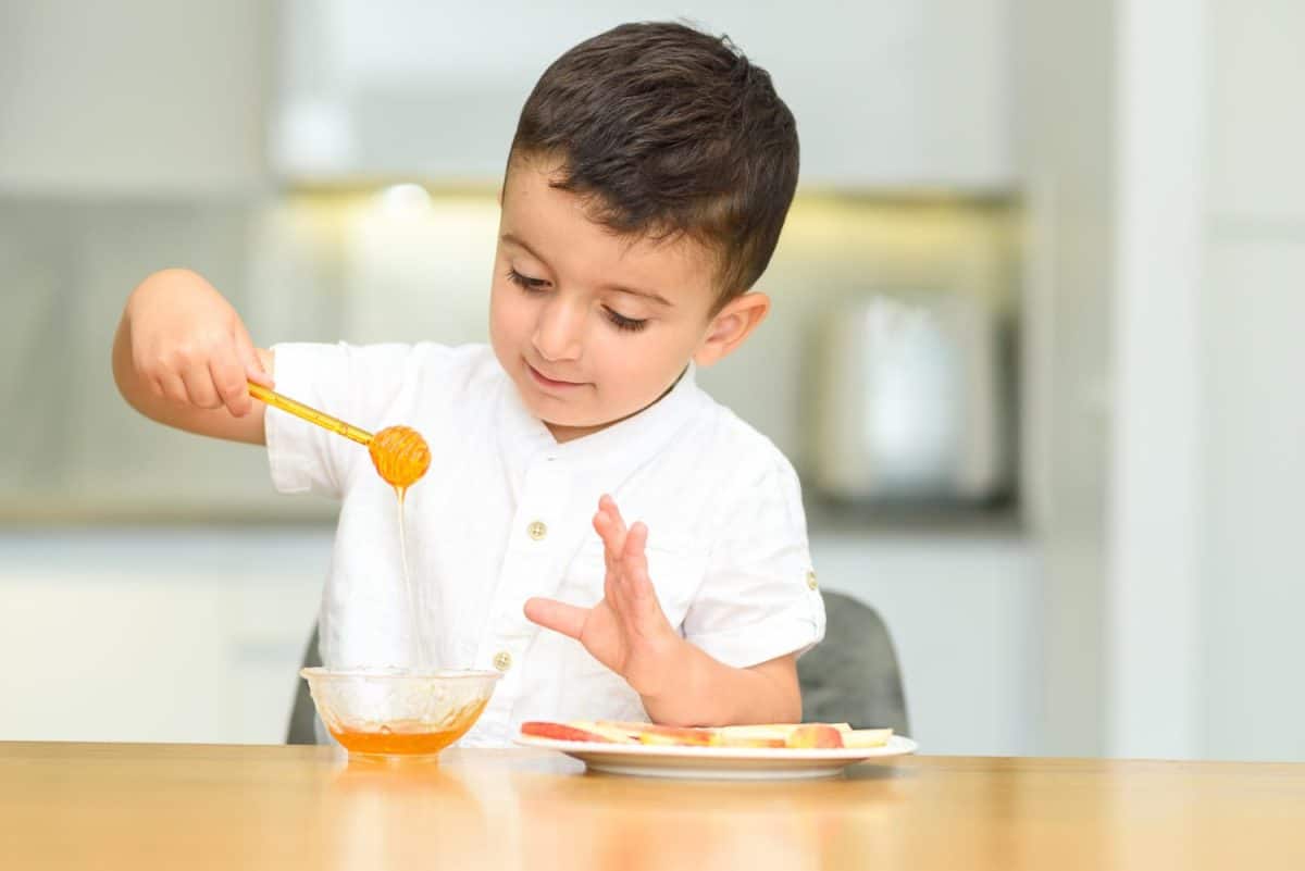 Little happy cute boy eating apple with honey, holding honey dipper. Child is having fun, celebrate Jewish New Year Rosh Hashanah.