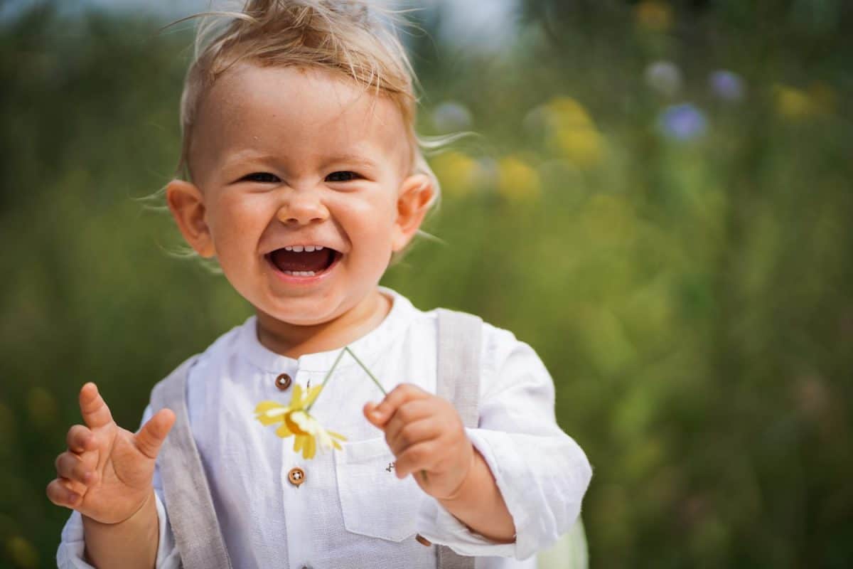 one year old happy blond german baby boy in white shirt playing outside in the garden with a yellow flower to send love or congratulate for birthday