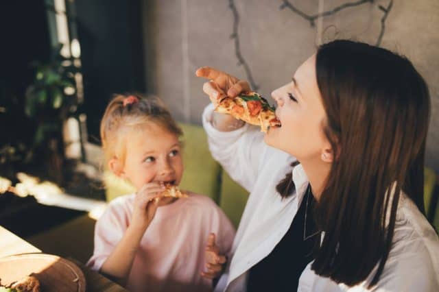 Happy mother and daughter eat pizza in a cafe and having fun.