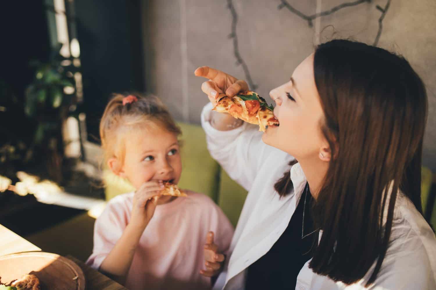 Happy mother and daughter eat pizza in a cafe and having fun.