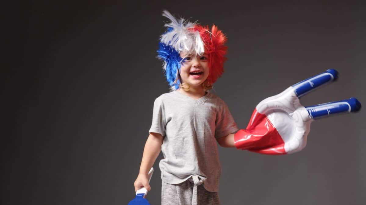 Young girl with a mohawk on his head in the color of the French flag supports his sports team. Football fan baby at the stadium rejoices at the victory of his team