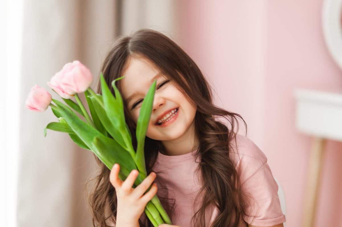 Portrait of a little girl with long dark hair close-up. The baby hugs a bouquet of fresh, delicate pink tulips. A gift for the holiday, spring time.