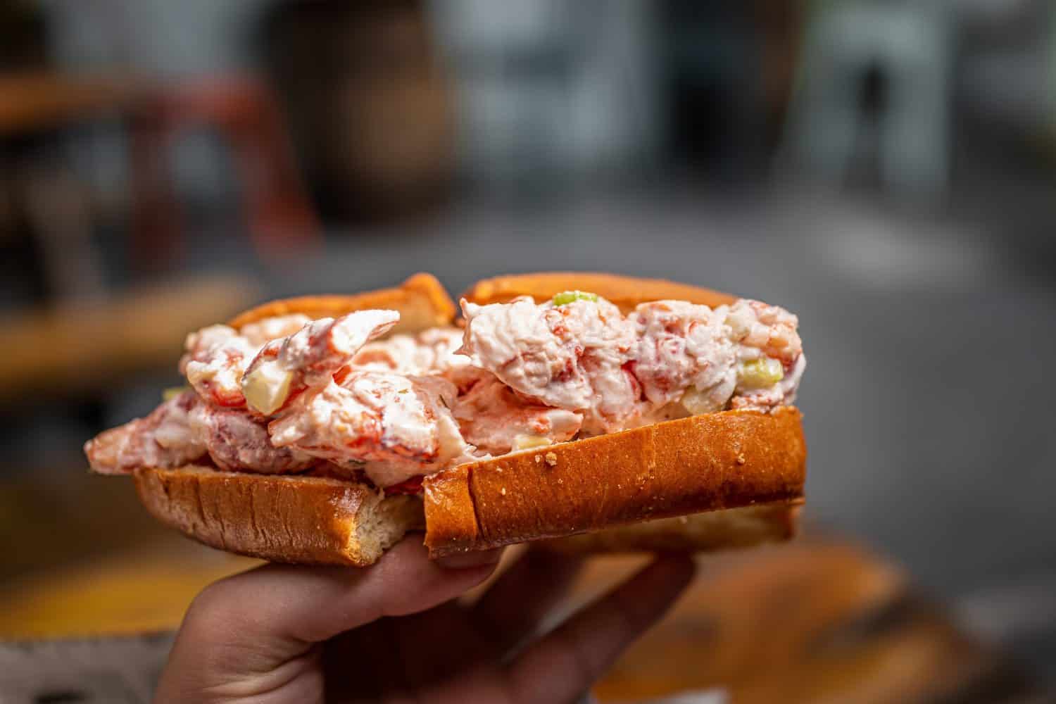 Maine lobster roll sandwich in brioche bun bread in seafood restaurant cafe in Key West, Florida with hand holding macro closeup