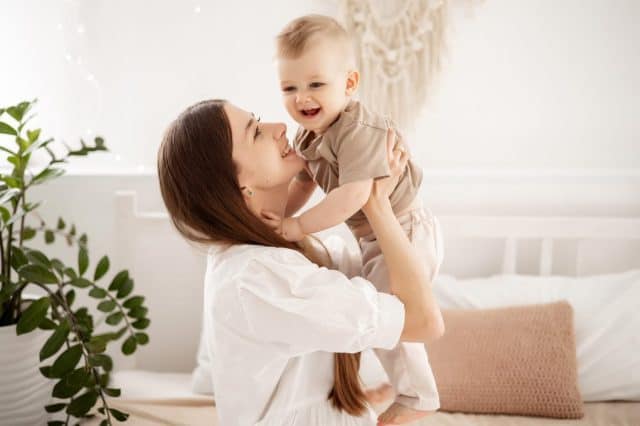 a young beautiful mother with a baby boy hugging on the bed at home in the bedroom, mother's care and love, portrait of a happy mother with a child, healthy motherhood