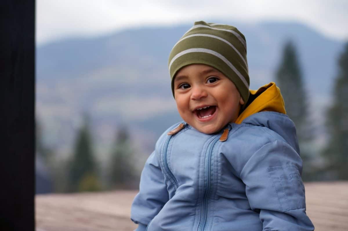 Cheerful cute baby boy laughing while sitting outdoor - happy adorable toddler smiling outdoors