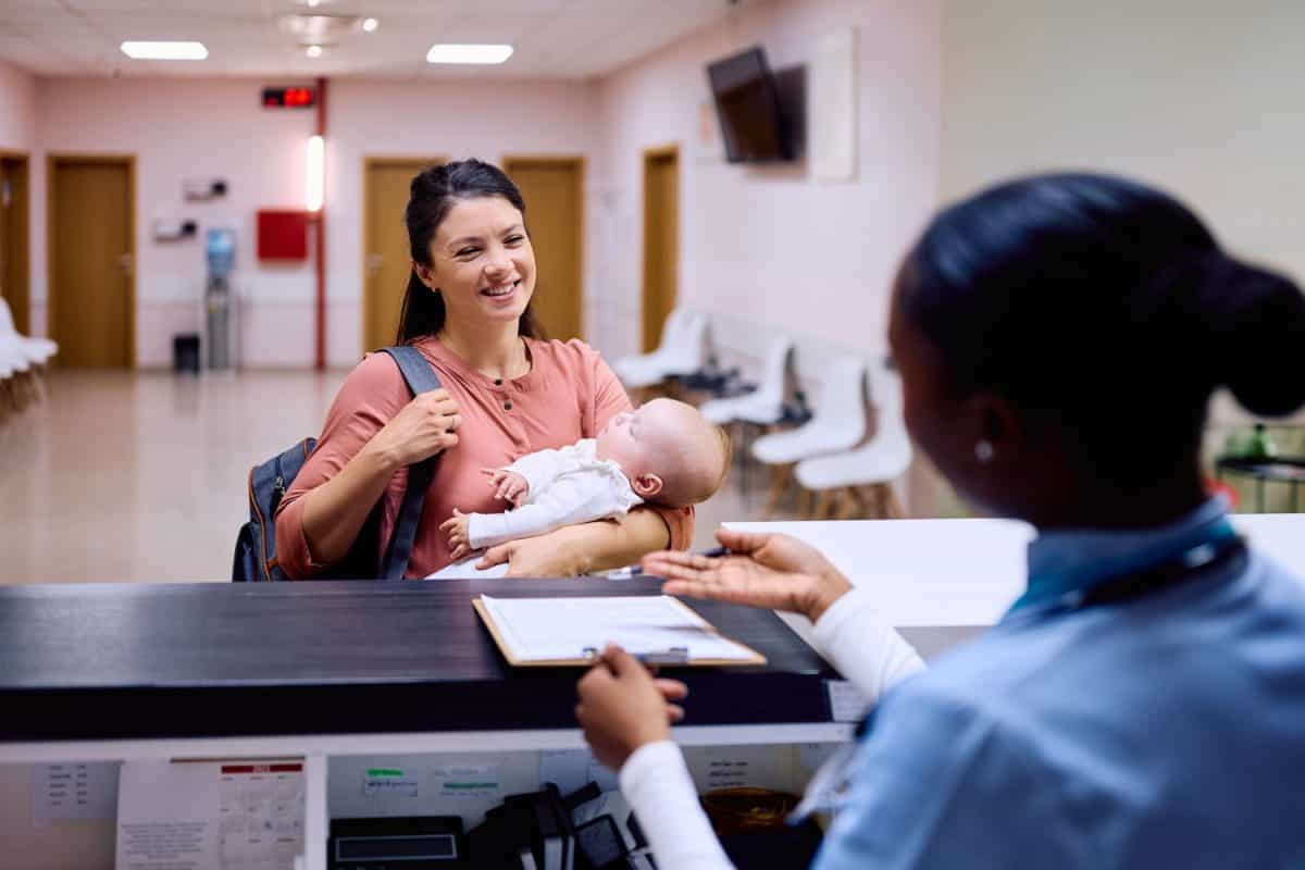 Happy mother with baby signing up for appointment at pediatrician's at medical clinic.