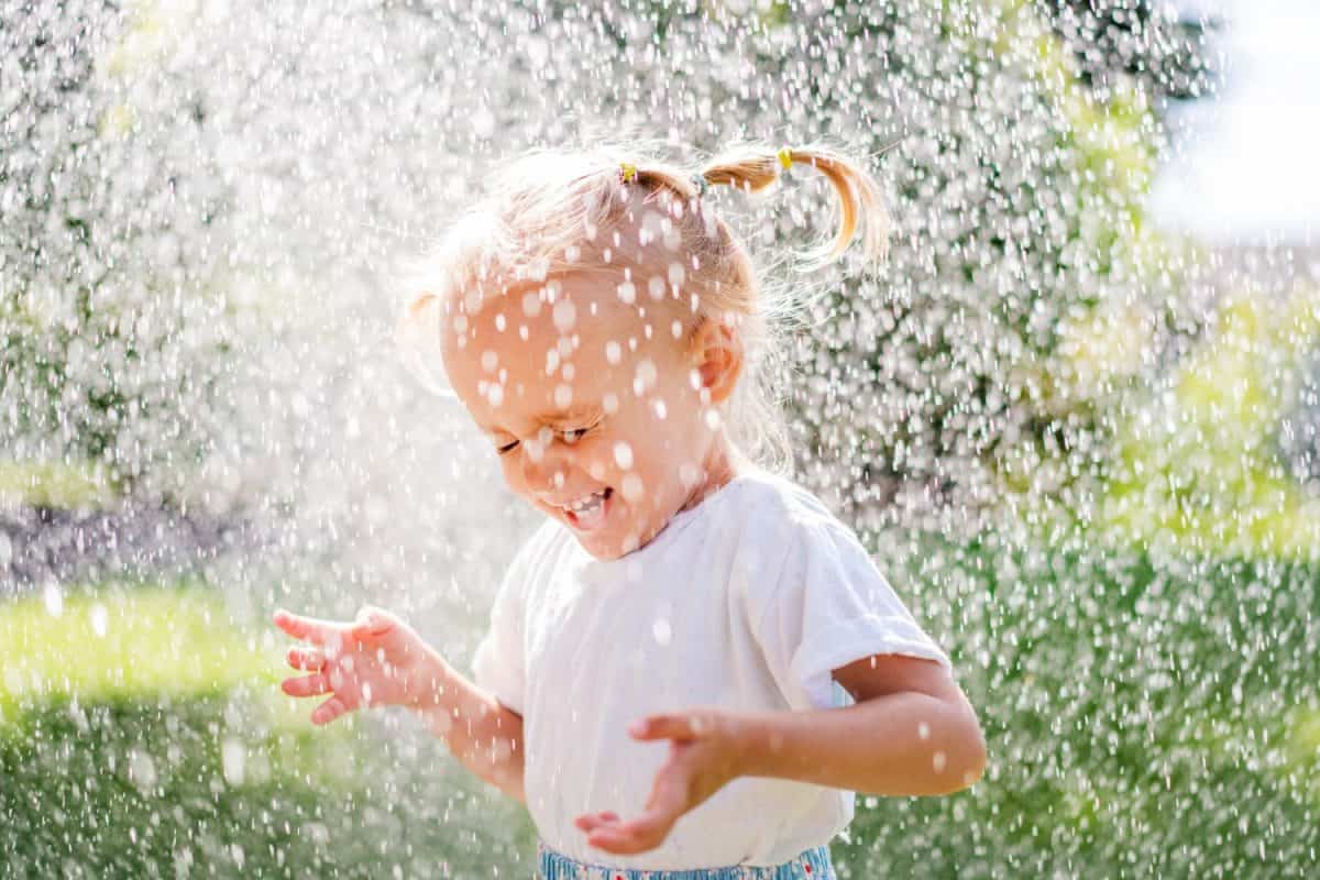 A beautiful girl in a dress plays on a green lawn and splashes with water