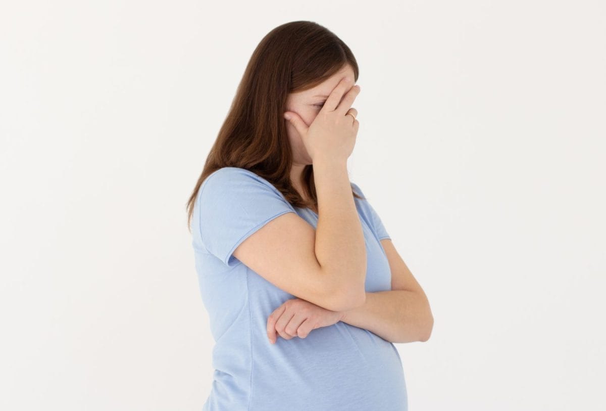 Embarrassed annoyed adult pregnant woman hiding face bend head down, facepalm, smirk irritated, not looking friend acting weird, feel humiliated uncomfortable, standing white background