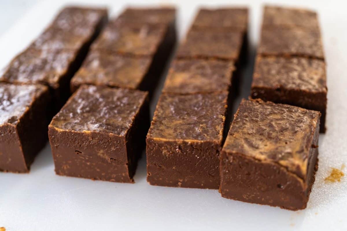 Cutting chocolate peanut butter fudge into small pieces on a white cutting board.