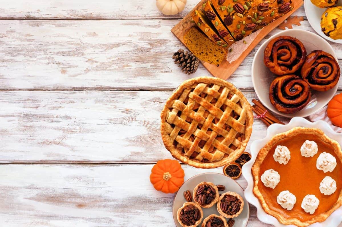 Autumn desserts side border. Table scene with an assortment of traditional fall sweet treats. Above view over a white wood background. Copy space.