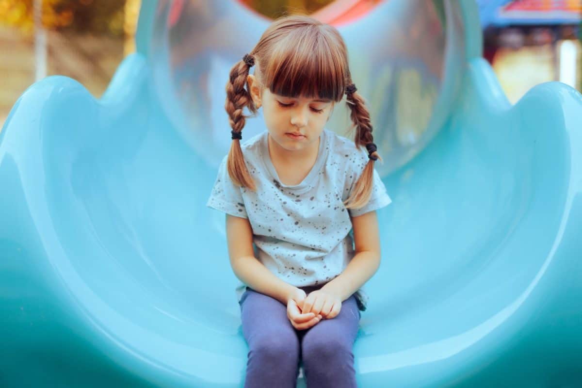 Sad Little Girl Sitting Alone in a Playground Slide. Timid anxious single child having none to play with