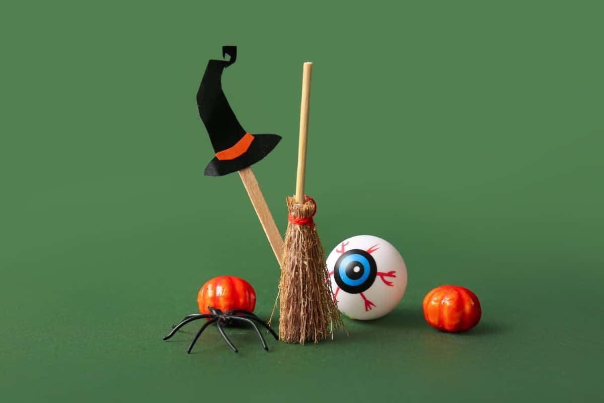 Halloween composition with broom, pumpkins, spider and eyeball on green background