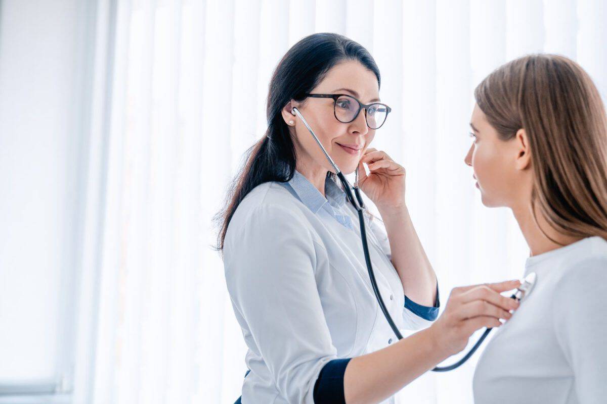 Female doctor listening to patients chest with stethoscope at the hospital, checking on lungs illnesses diseases. General practitioner listening to patient`s heart beat, cardiology concept