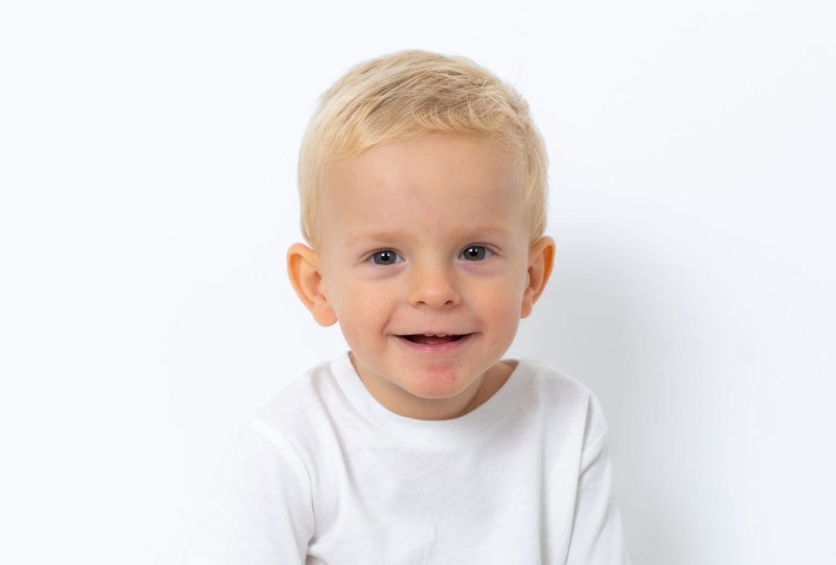 Cute beautiful blond two year old baby boy standing over white studio background and gesturing from happiness, dancing and playing.