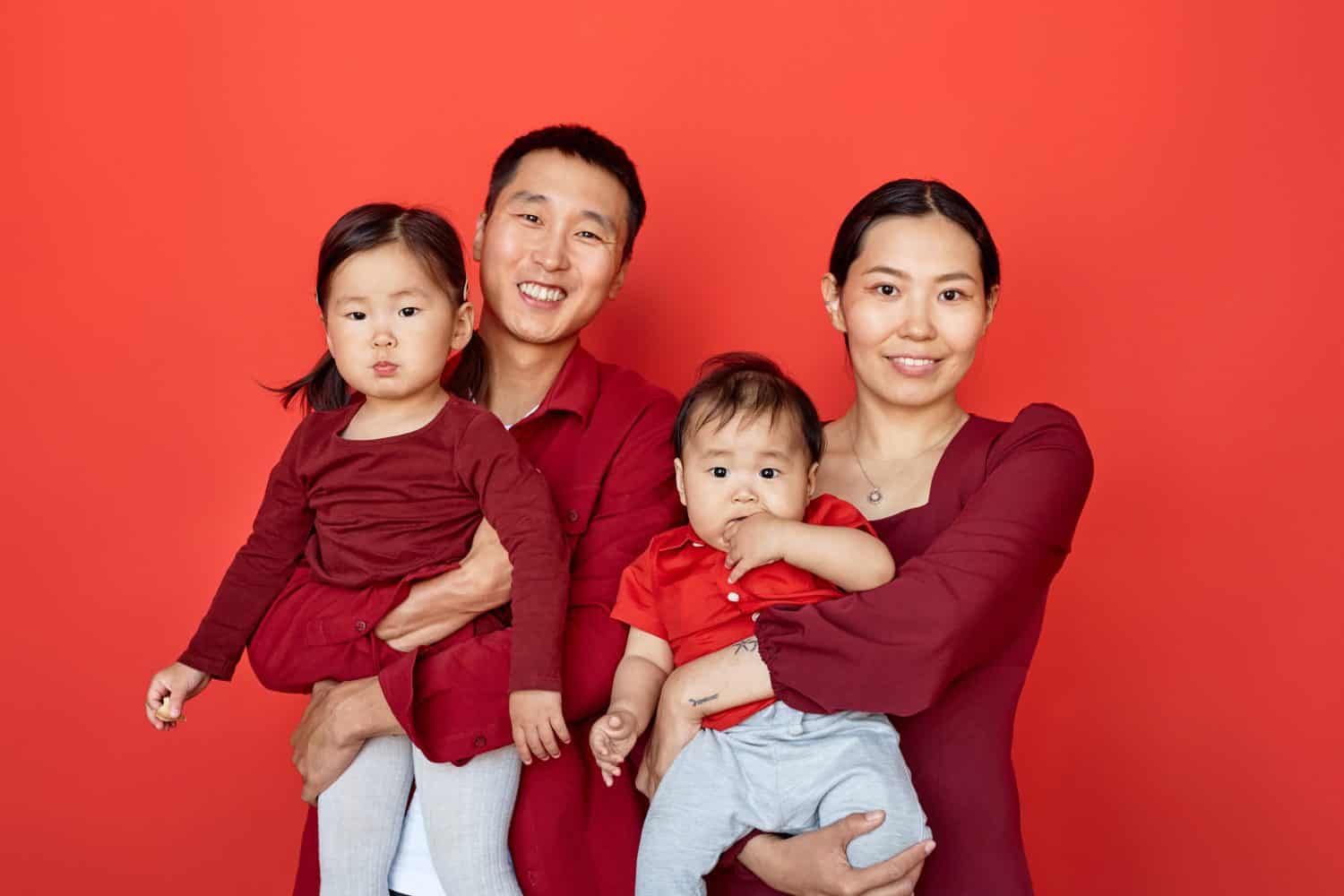 Waist up portrait of happy Chinese family wearing red posing with two children on red background all smiling at camera