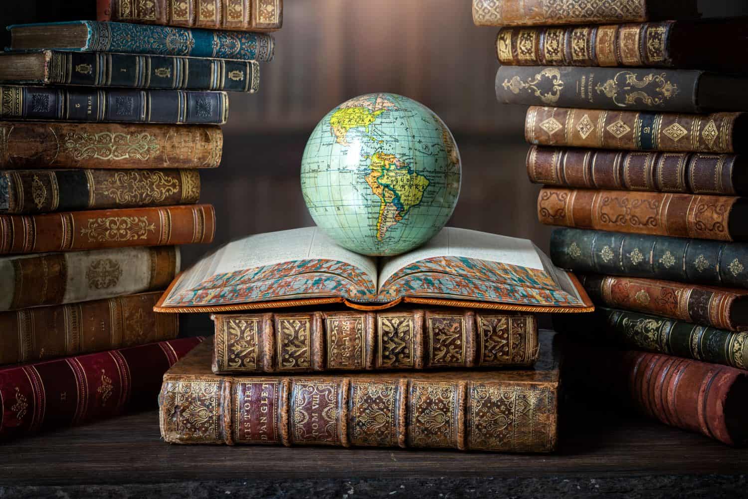 Old globe lying on an open book in a library. Conceptual background on history, education, literature topics. Translation of book titles - history of England, ancient history.