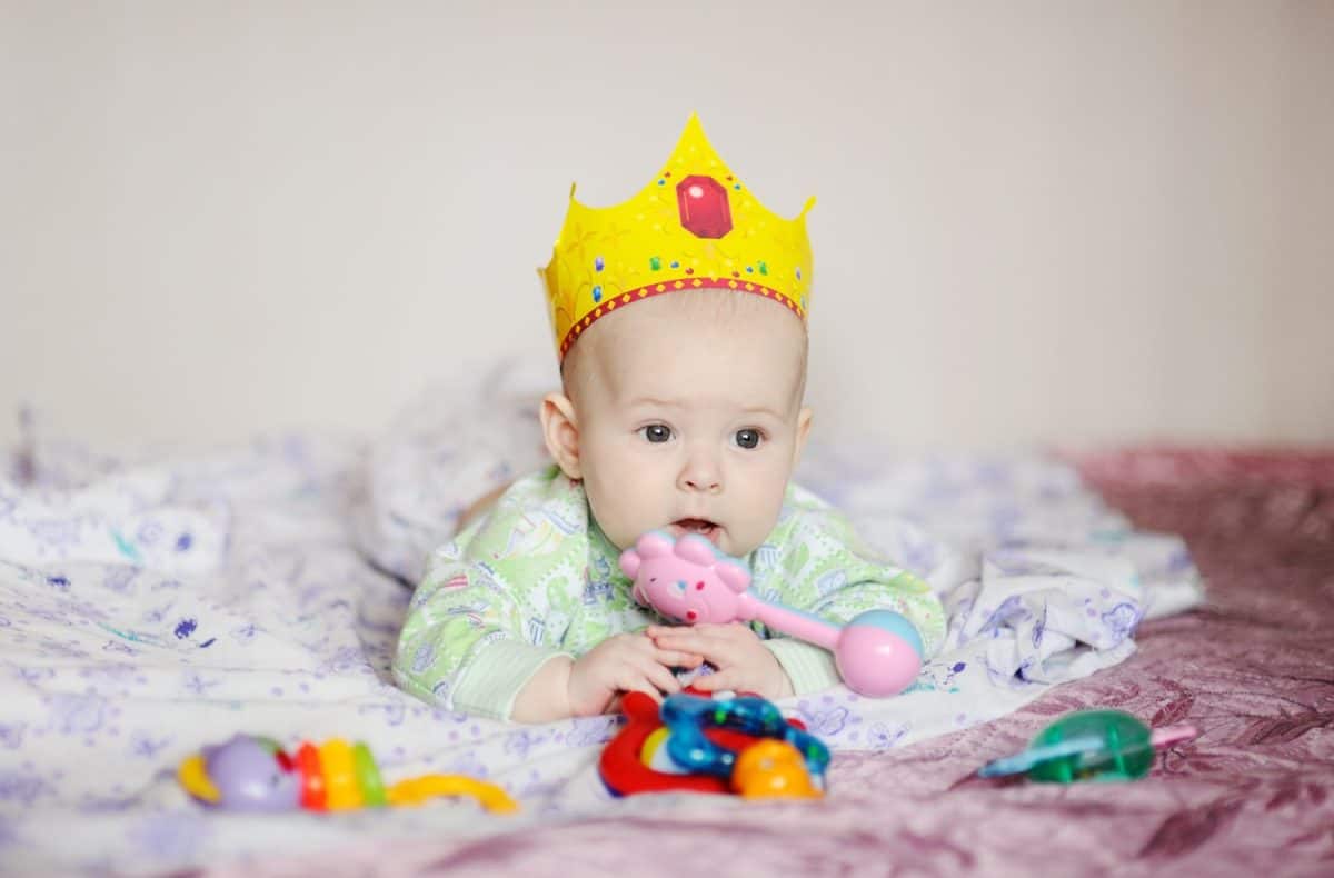 child in the crown lies on a bed with toys