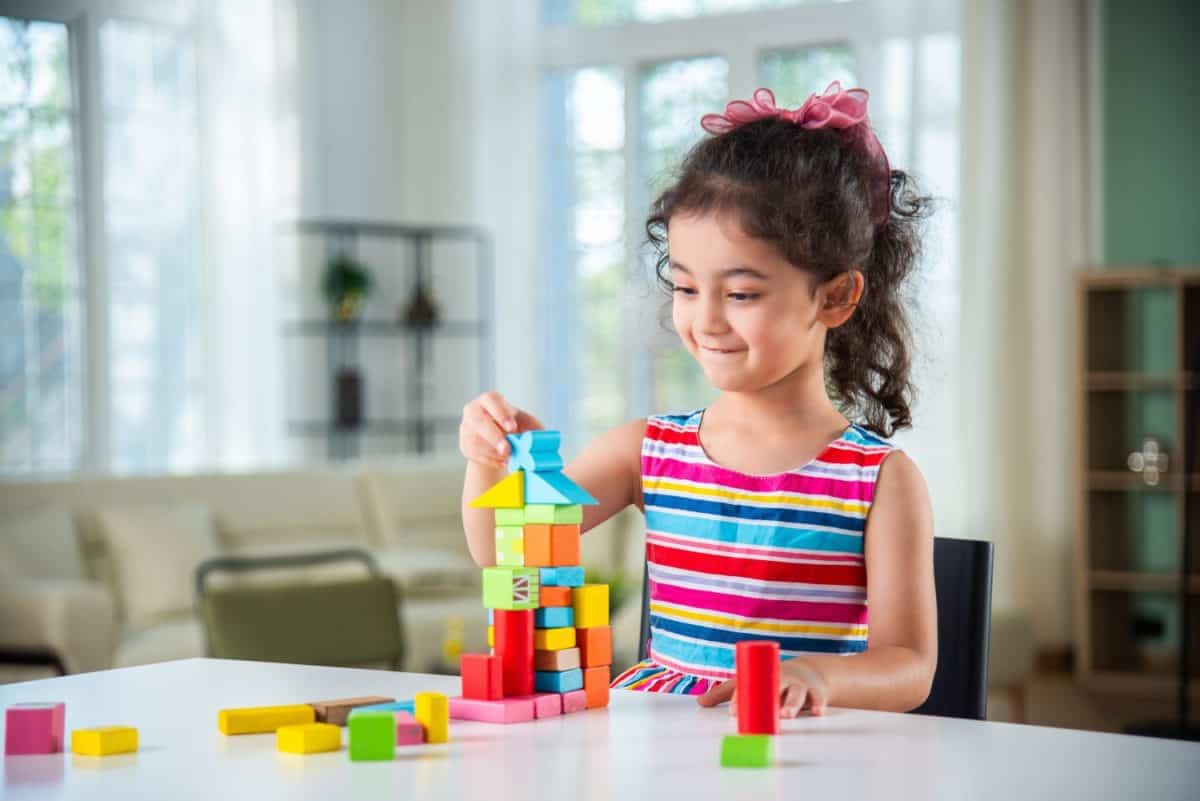 Indian little girl playing with wooden blocks toys on the table at home