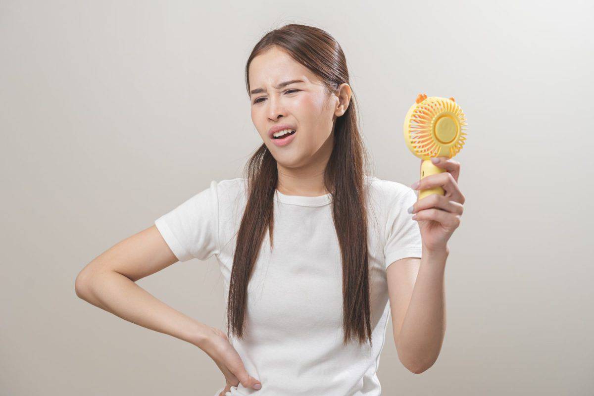 Suffering summer heat wave stroke, hot weather, tired asian young woman sweaty and thirsty, refreshing with hand in blowing, wave fan to ventilation when temperature high, isolated on background.