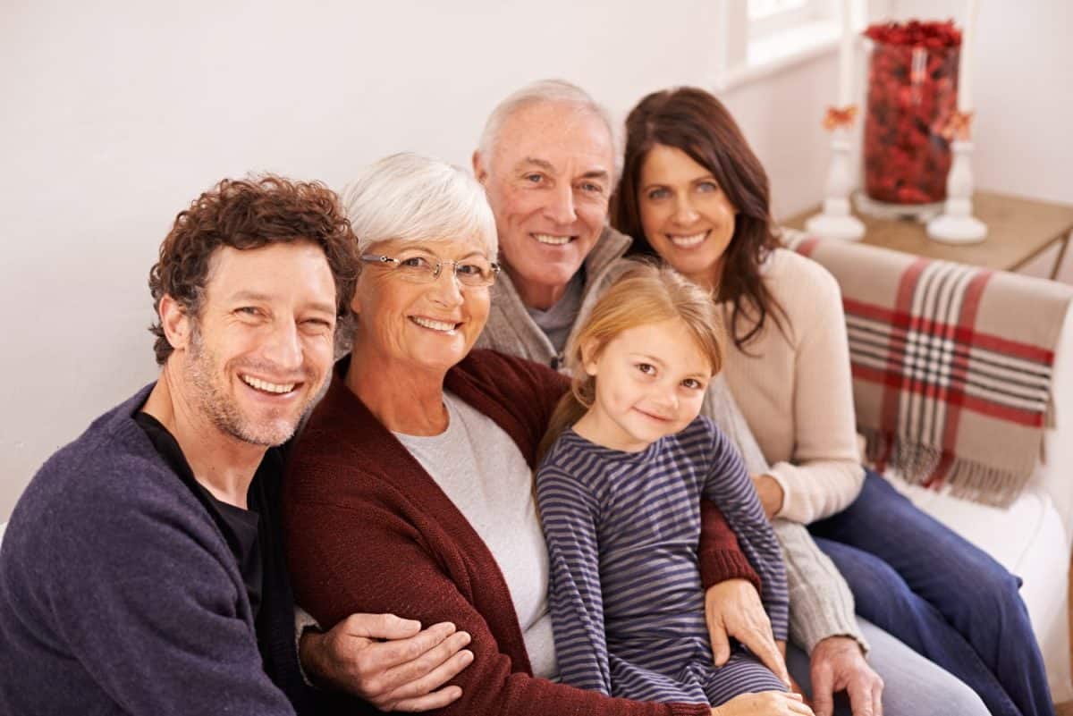 Grandparents, parents and kid on sofa for portrait with hug, care or love with generations for bonding in home. Mother, father and senior people with child for embrace on lounge couch in family house