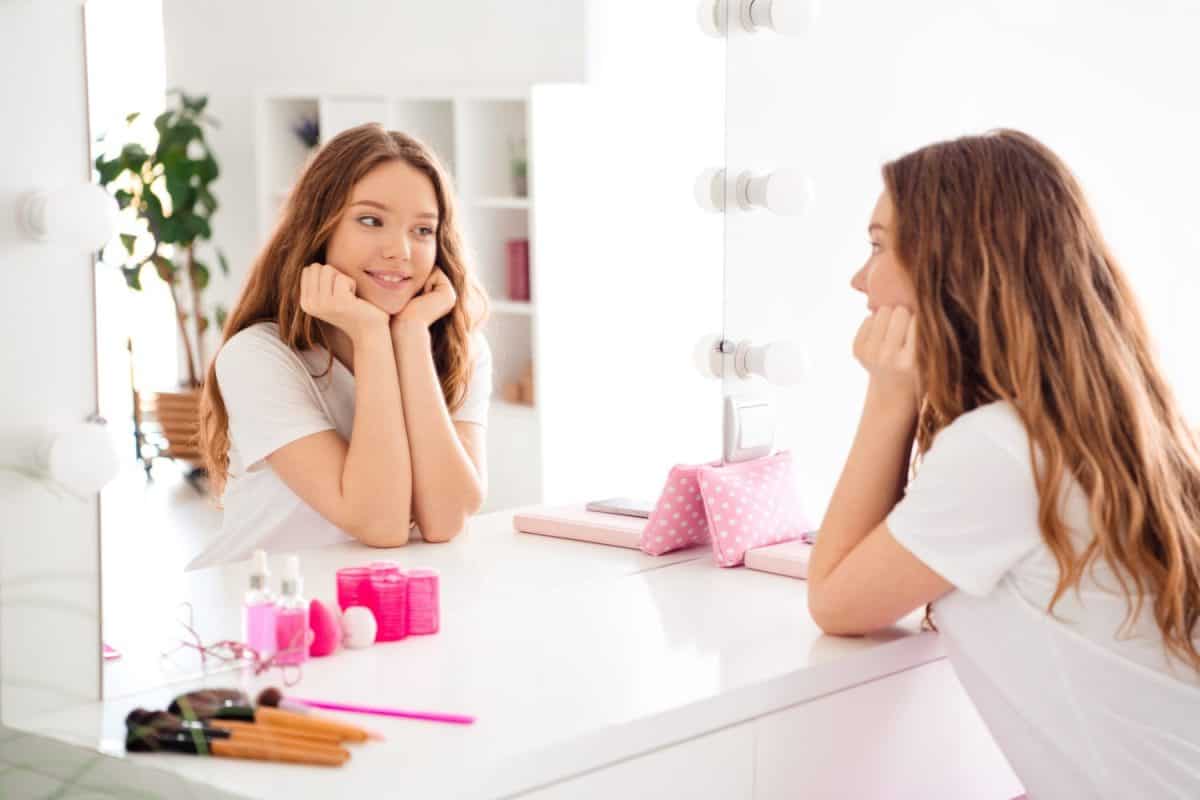 Portrait of cute cheerful peaceful female person hands touch cheeks look mirror reflection bright interior bedroom inside