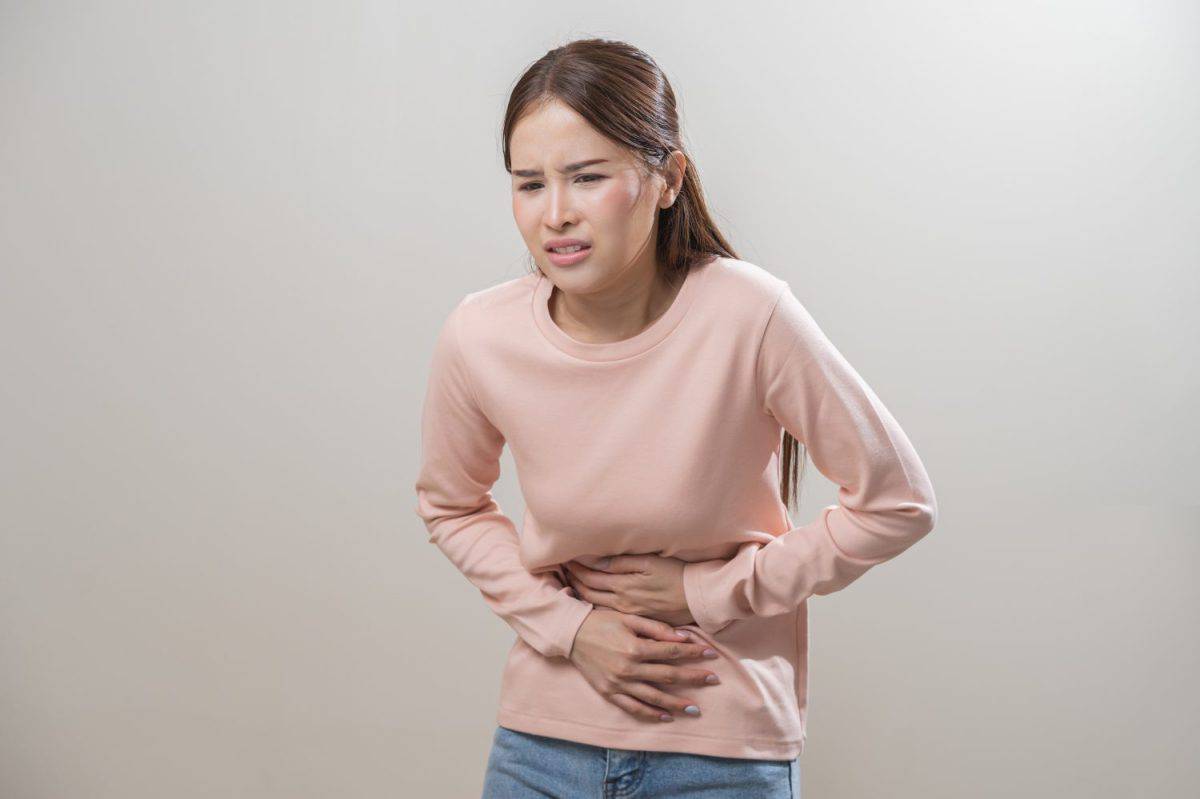 Flatulence asian young woman intolerance hand in stomach ache, suffer from food poisoning, abdominal pain and colon problem, gastritis or diarrhoea when at home. Patient belly, abdomen or inflammation