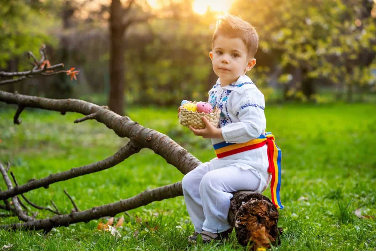 Cute little boy posing in romanian traditional costume with dye colored Easter Eggs in a park and cherry blossom