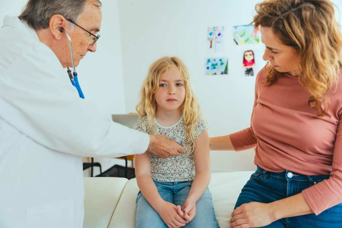 Professional doctor checking child during medical checkup in clinic office - Pediatrician using stethoscope to examine breathing and heartbeat of young patient - Health care and medicine concept