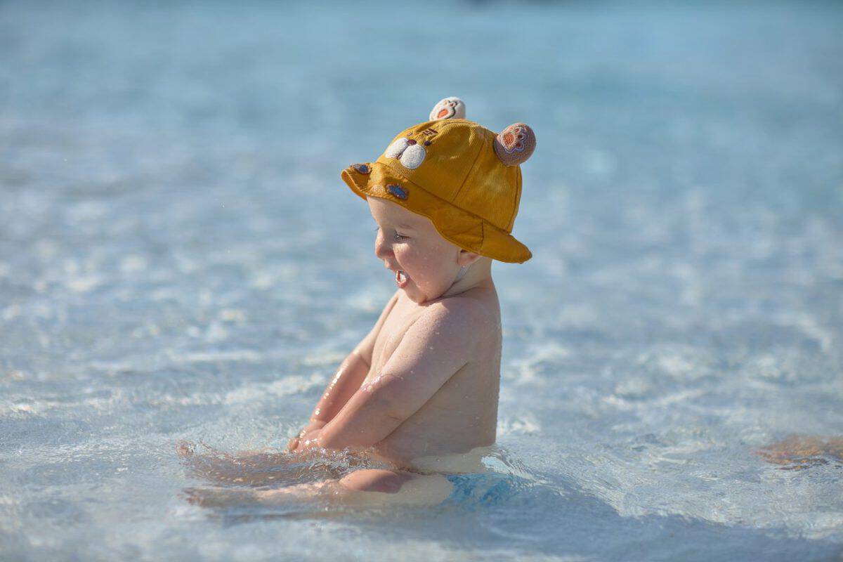 a little half a year old, a baby baby crawling on the water, smiling, outdoors, in a panama hat, in diapers, in the sun at the resort.