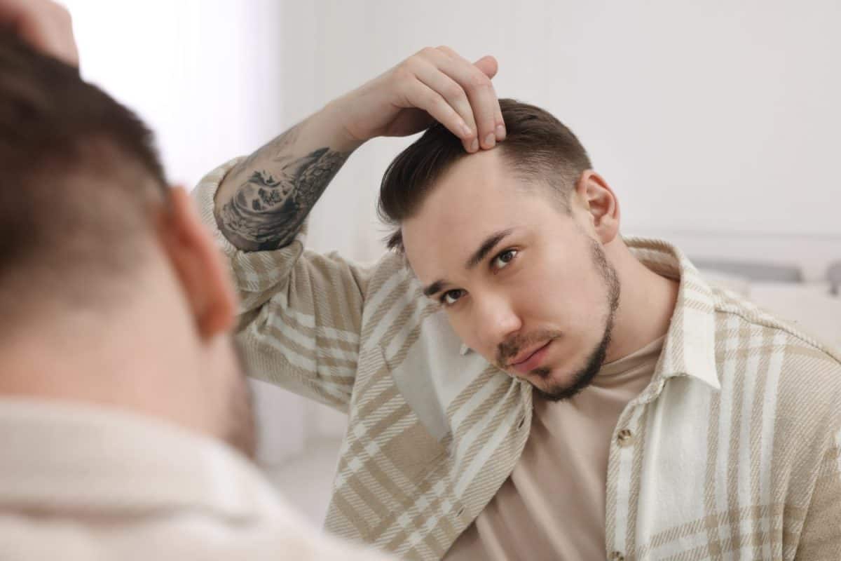 Baldness concept. Sad man with receding hairline looking at mirror indoors