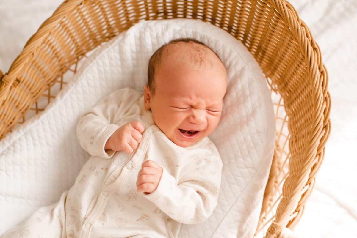 Crying baby boy with colic stomach pain in straw crib close up top view.