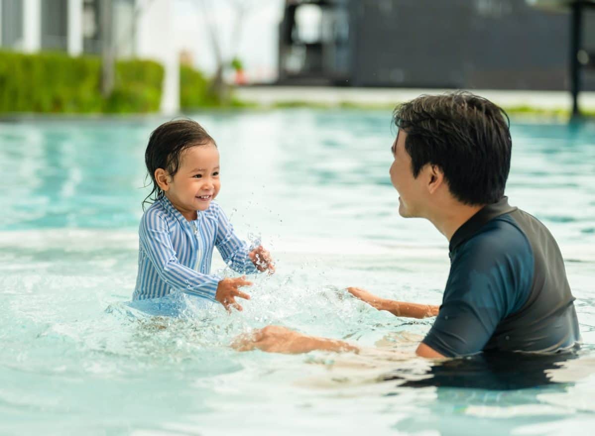 happy father with todler baby playing water splashing in a swimming pool