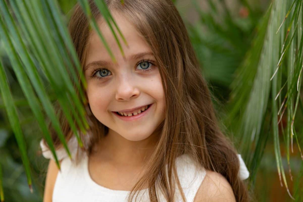 The face of a little girl surrounded by tropical leaves. Closeup portrait of a beautiful child with perfect skin and dark hair. Natural cosmetics, health, cleanliness, skin care, beauty concept