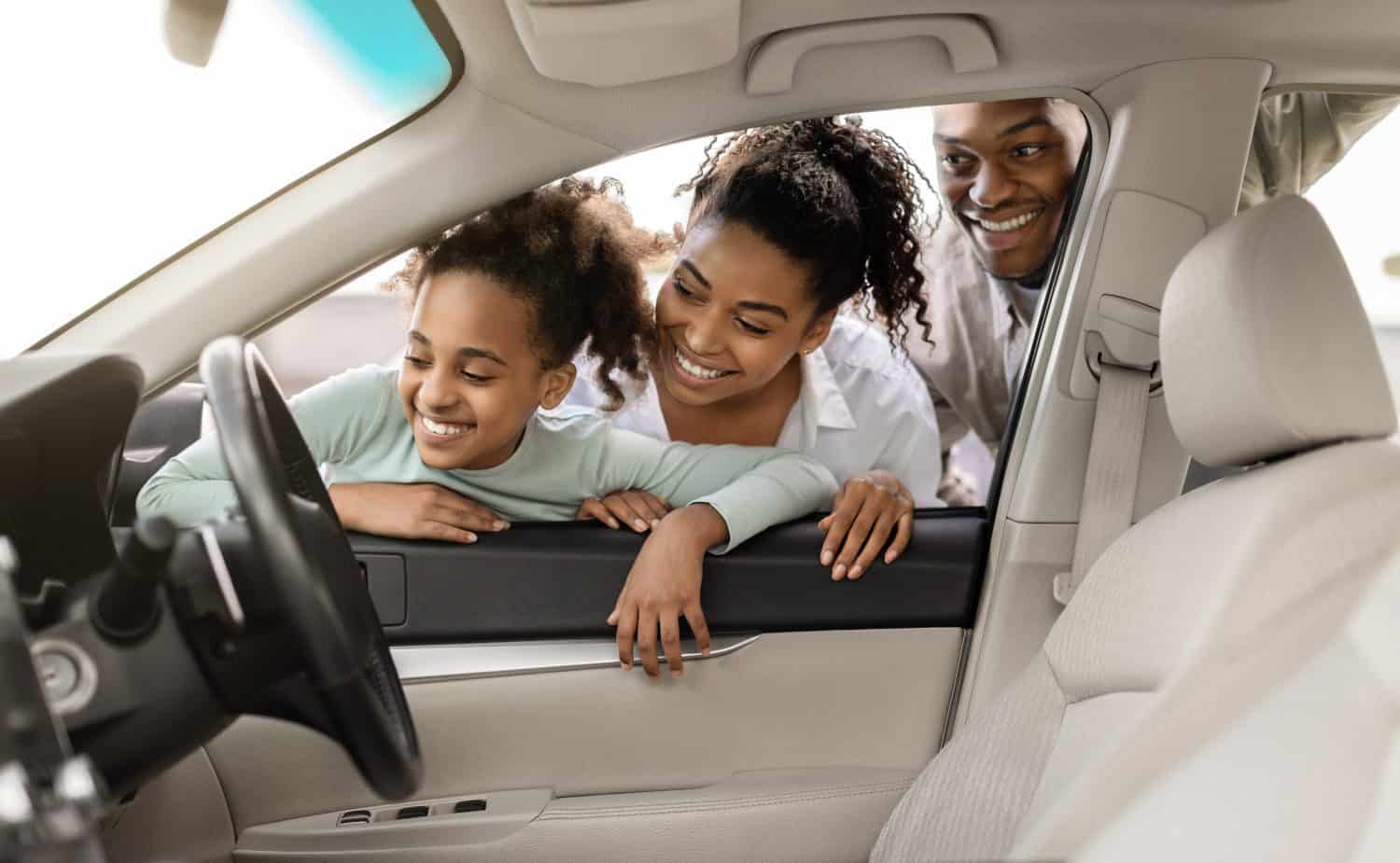 Cheerful Black Family Of Three Buying New Car, Looking Through Window At Auto Interior Choosing Luxury Automobile In Dealership. Vehicle Rent And Purchase Concept