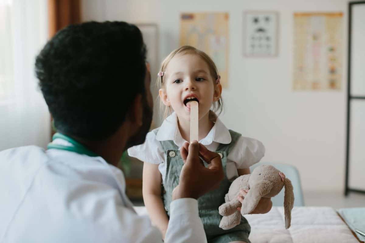 Male Pediatrician examining throat of a little ill girl.