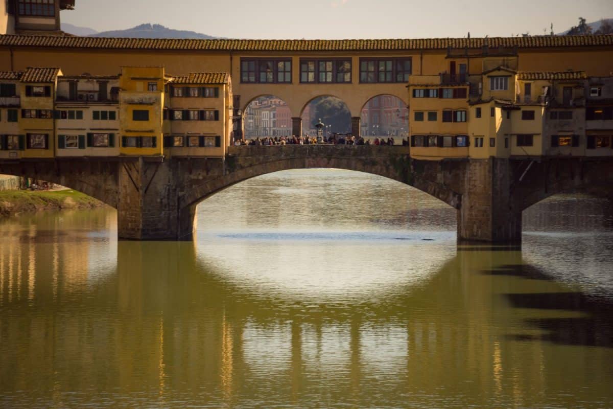 View of the historic Ponte Vecchio bridge reflecting on the Arno River in Florence, Italy, during sunset.