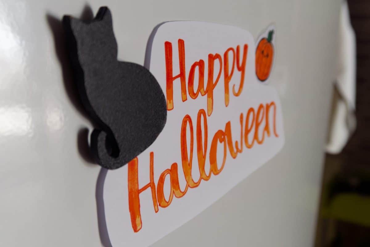 Happy Halloween paper sign with black cat magnet and cute pumpkin sticker on fridge