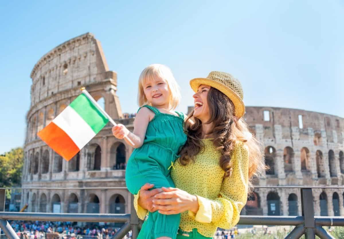 Happy mother and baby girl with italian flag in front of colosseum in rome, italy