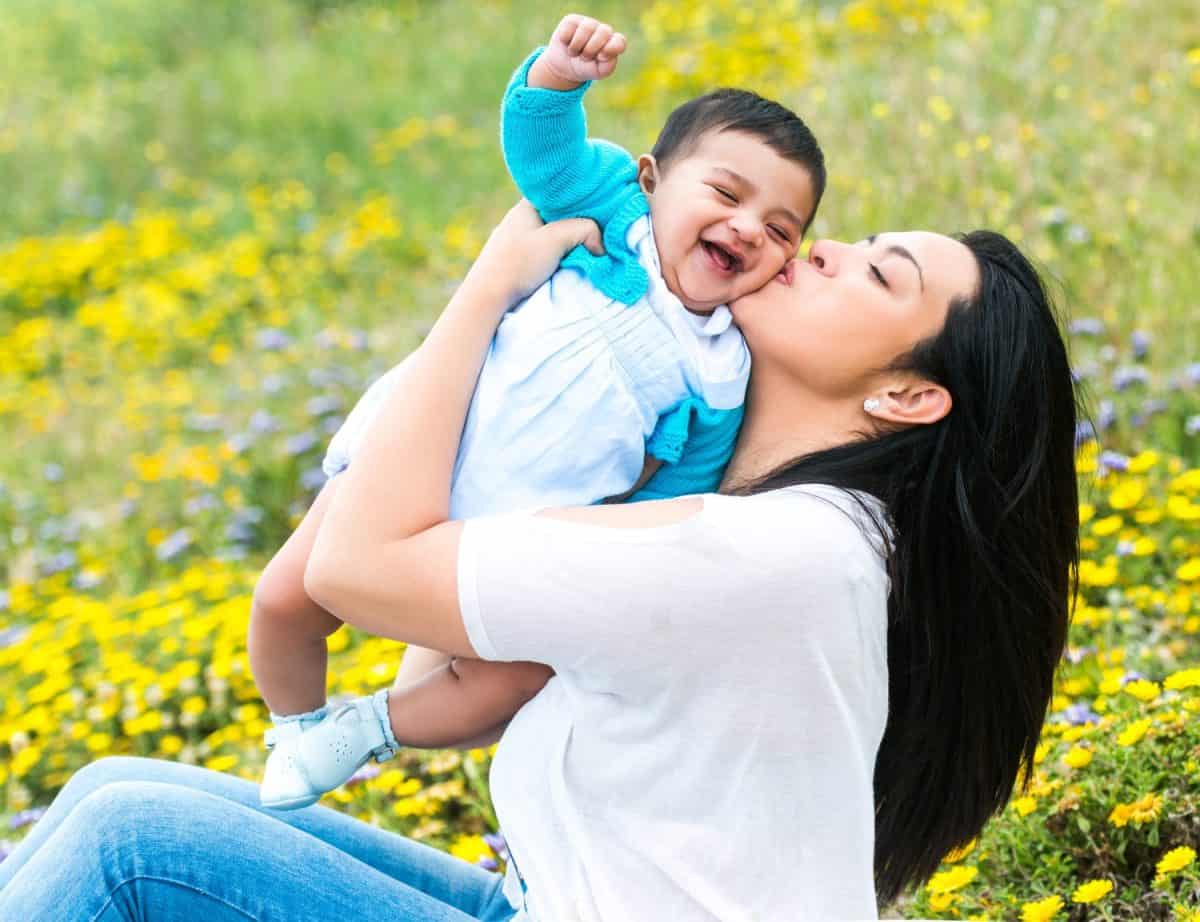 beautiful mother playing with her baby boy on the meadow in summer day