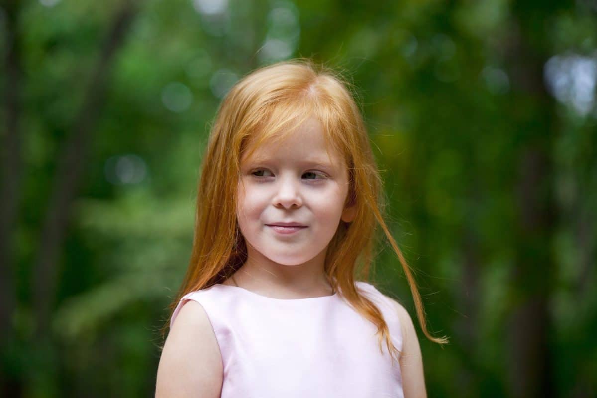 Portrait of a little red-haired girl on the background of summer green forest