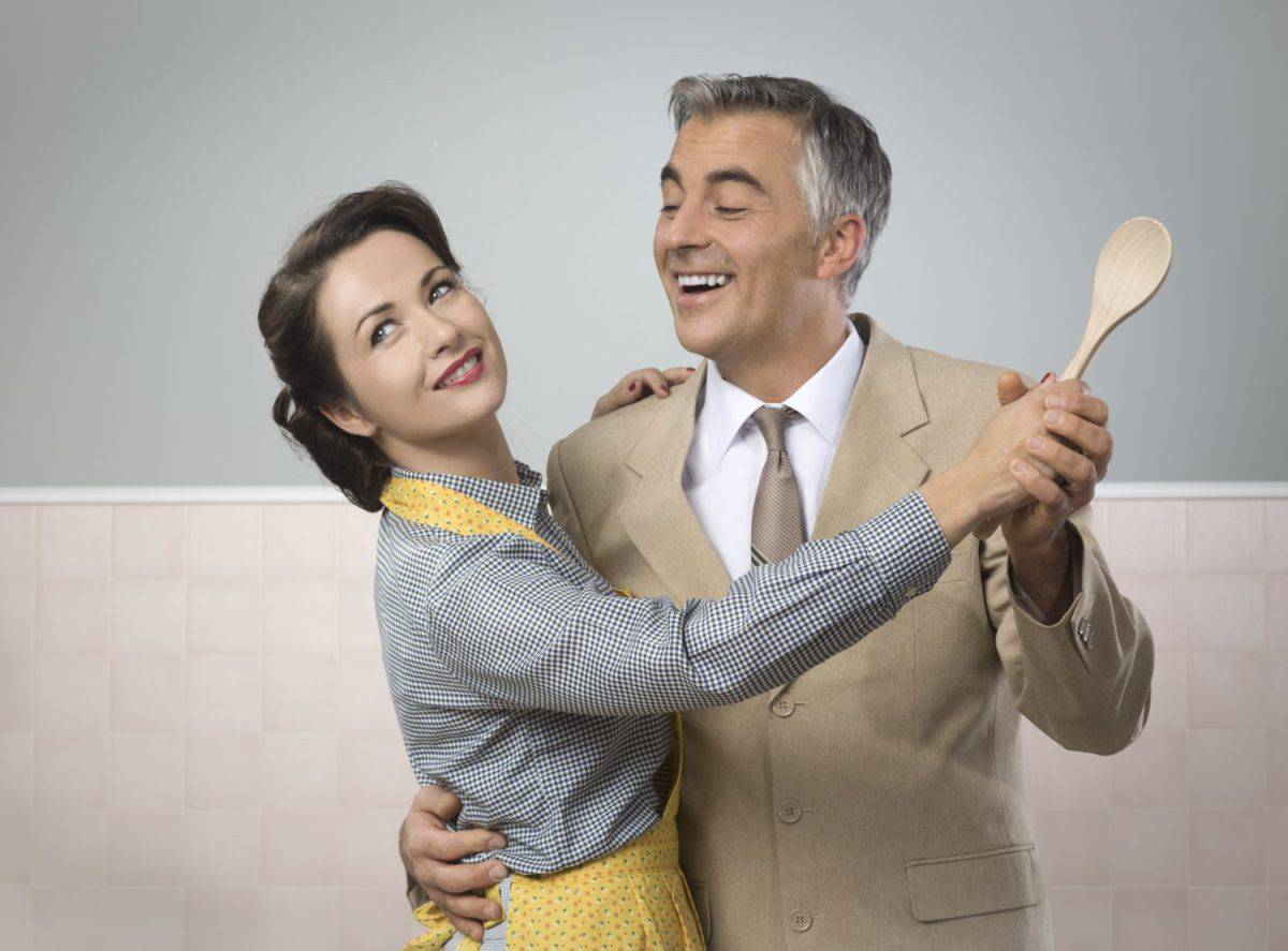 Smiling vintage couple dancing in the kitchen and holding a wooden spoon