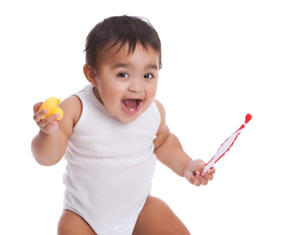 Adorable mixed race baby boy holding an infant toothbrush and rubber duckie. Isolated on white.